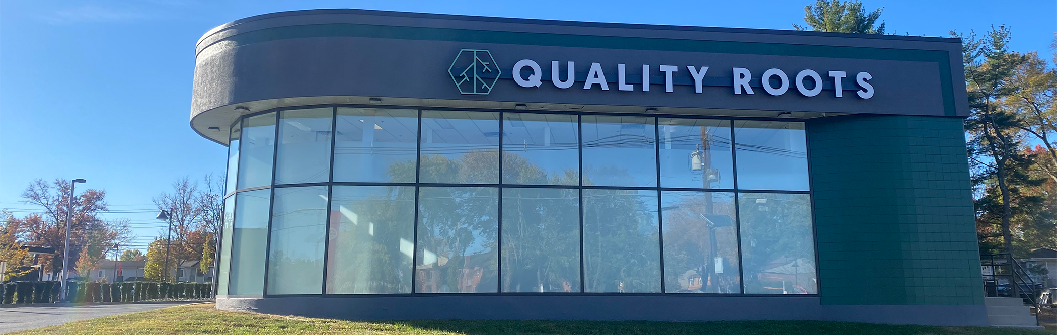 Quality Roots storefront in Marlton, New Jersey, featuring a modern curved glass exterior with the company’s logo and signage under a clear blue sky.